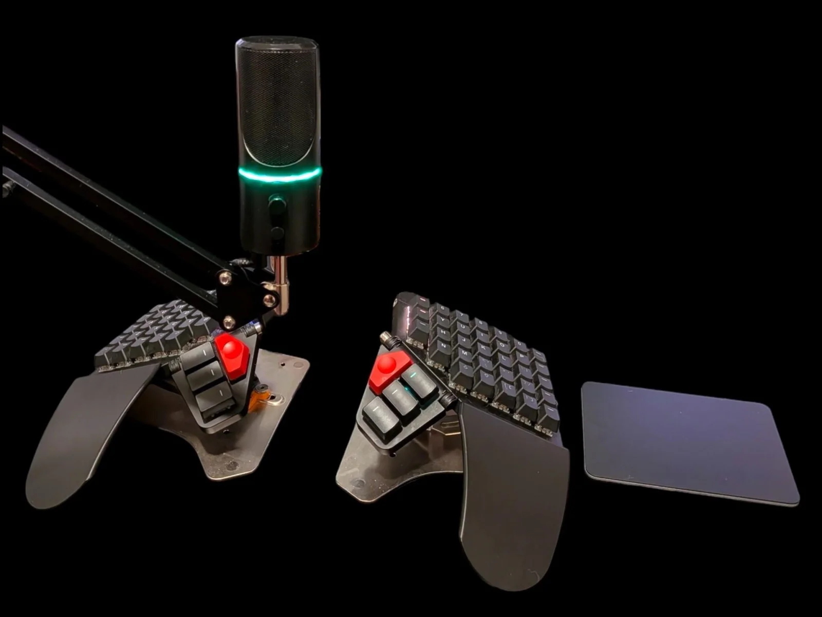 My desk: a microphone on a boom arm, a split mechanical keyboard with red thumb domes, and an Apple Magic Trackpad on a black surface